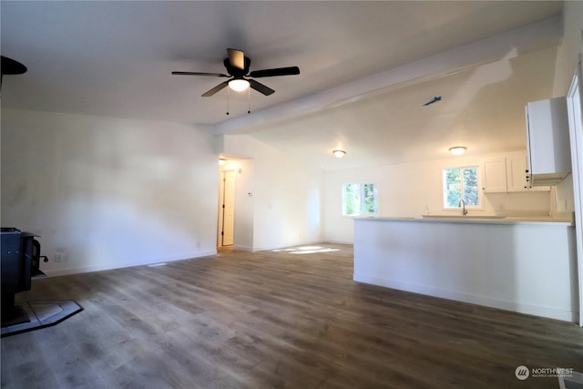 unfurnished living room with a wood stove, ceiling fan, sink, lofted ceiling with beams, and hardwood / wood-style flooring