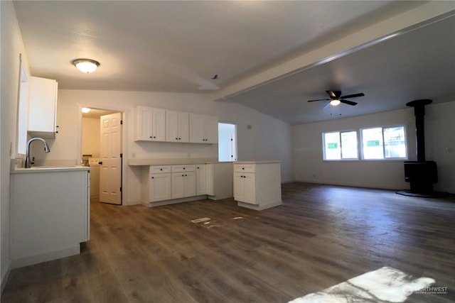 kitchen with a wood stove, ceiling fan, dark wood-type flooring, vaulted ceiling with beams, and white cabinets