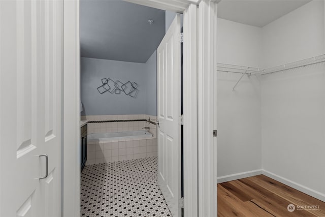 bathroom with wood-type flooring, vanity, and tiled tub