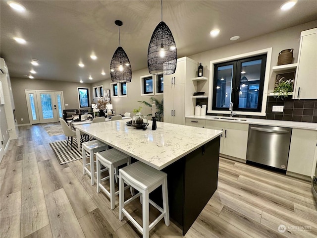 kitchen featuring stainless steel dishwasher, decorative light fixtures, a kitchen island, white cabinetry, and sink