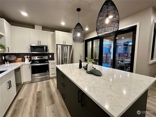 kitchen with a kitchen island, appliances with stainless steel finishes, pendant lighting, and white cabinetry