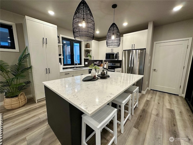 kitchen featuring appliances with stainless steel finishes, a kitchen island, white cabinets, decorative light fixtures, and sink