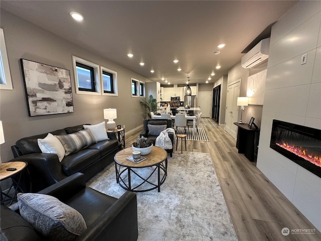 living room featuring a tiled fireplace, light hardwood / wood-style flooring, and a wall mounted AC