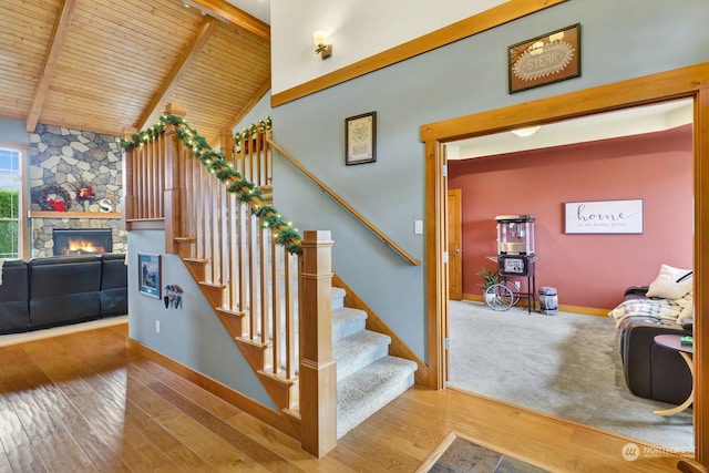 stairway featuring a stone fireplace, beamed ceiling, high vaulted ceiling, wood-type flooring, and wood ceiling