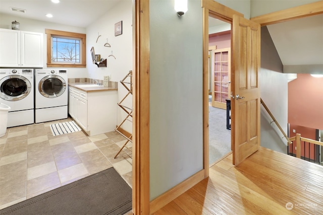 laundry area featuring washing machine and clothes dryer, sink, cabinets, and light wood-type flooring