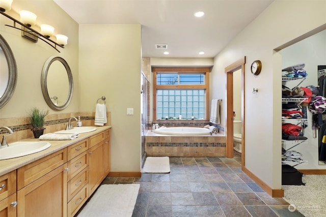 bathroom featuring tiled tub, vanity, and toilet