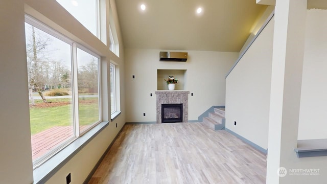 unfurnished living room with a wall unit AC, a healthy amount of sunlight, and light hardwood / wood-style floors