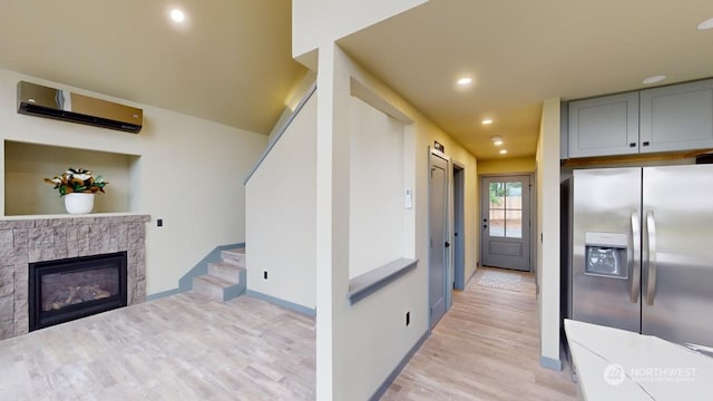 kitchen with gray cabinetry, an AC wall unit, stainless steel fridge, light hardwood / wood-style floors, and a fireplace