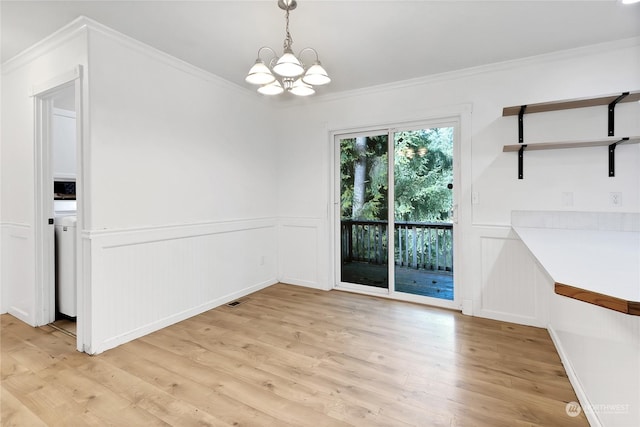 22222 Bluewater Dr SE, Yelm, WA 98597 - unfurnished dining area featuring a chandelier, crown molding, light wood-style floors, wainscoting, and a decorative wall