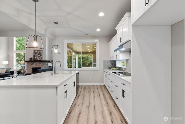 kitchen with a kitchen island with sink, sink, decorative light fixtures, light hardwood / wood-style flooring, and white cabinets