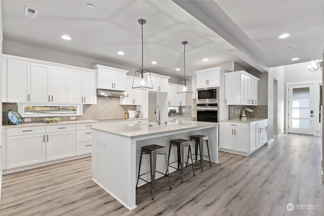 kitchen with pendant lighting, light hardwood / wood-style flooring, an island with sink, white cabinetry, and stainless steel appliances