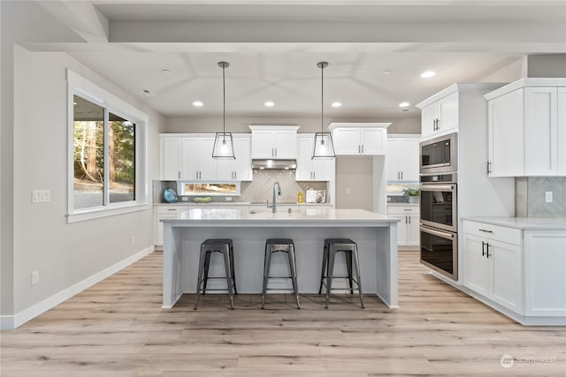 kitchen featuring stainless steel appliances, pendant lighting, light hardwood / wood-style floors, white cabinetry, and an island with sink