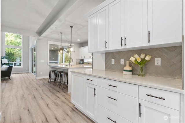 kitchen with hanging light fixtures, a kitchen breakfast bar, backsplash, white cabinets, and light wood-type flooring