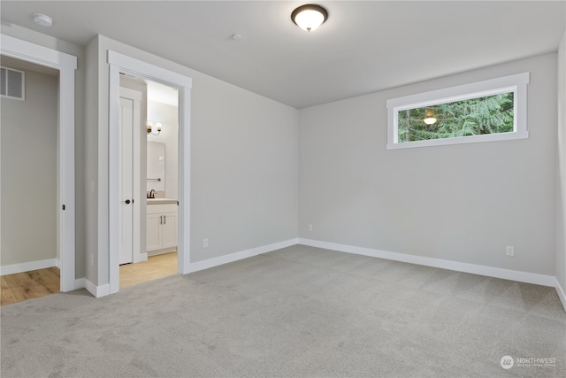 unfurnished bedroom featuring light carpet, connected bathroom, and sink