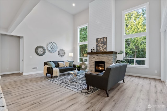 living room with a stone fireplace, a high ceiling, and light hardwood / wood-style flooring