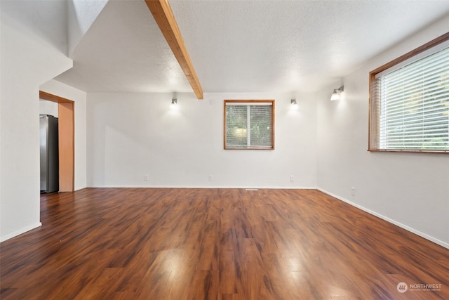 empty room with beamed ceiling, a textured ceiling, and dark hardwood / wood-style floors