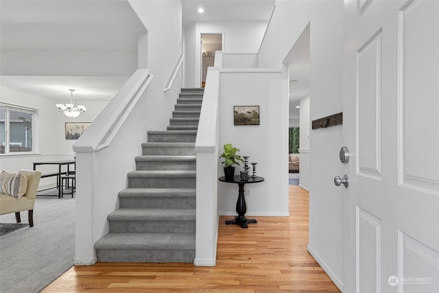 stairs with wood-type flooring and a notable chandelier