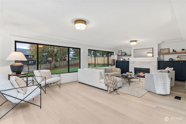 living room with light wood-type flooring, a healthy amount of sunlight, and a brick fireplace