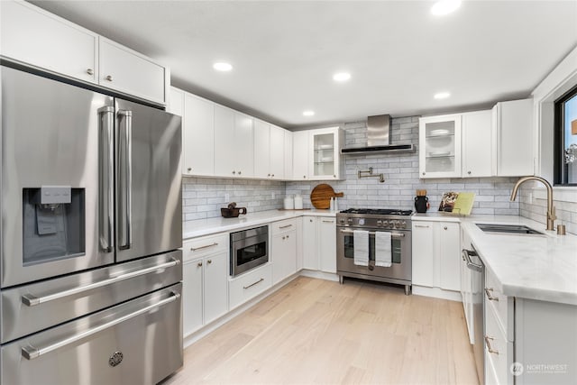 kitchen featuring stainless steel appliances, wall chimney exhaust hood, white cabinetry, and sink