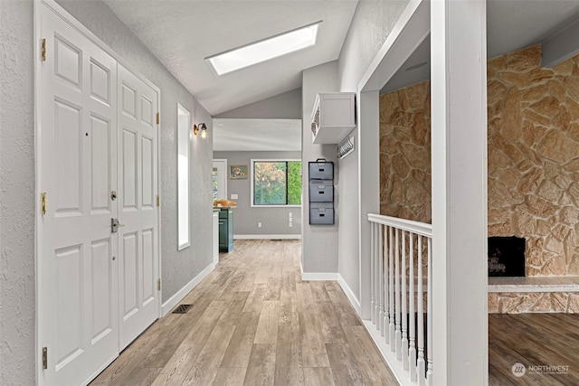 hallway with a textured ceiling, lofted ceiling, and light wood-type flooring