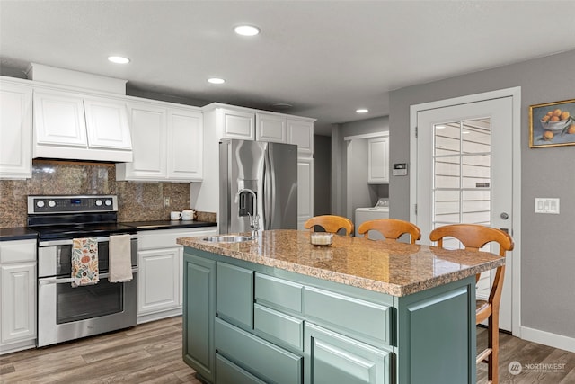 kitchen with stainless steel appliances, a kitchen island with sink, sink, washer / clothes dryer, and white cabinetry