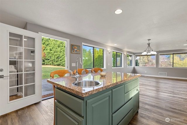 kitchen featuring a healthy amount of sunlight, sink, wood-type flooring, and an island with sink