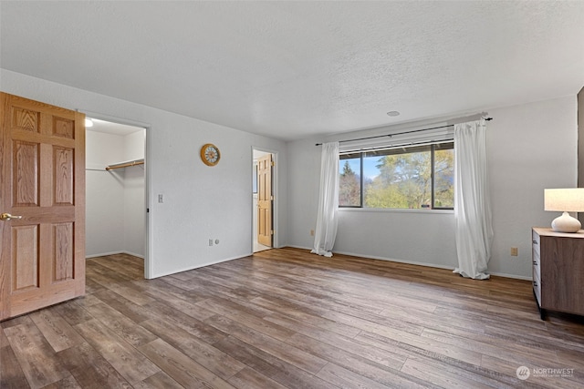 unfurnished bedroom featuring light hardwood / wood-style floors, a walk in closet, a textured ceiling, and a closet