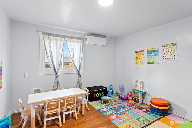 recreation room featuring wood-type flooring and an AC wall unit