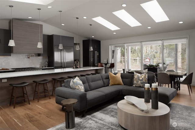 living room featuring vaulted ceiling with skylight, sink, and light hardwood / wood-style flooring