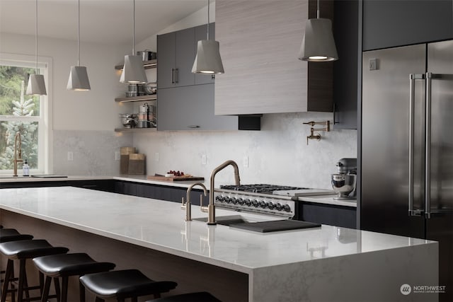 kitchen with sink, a kitchen breakfast bar, light stone countertops, built in refrigerator, and pendant lighting