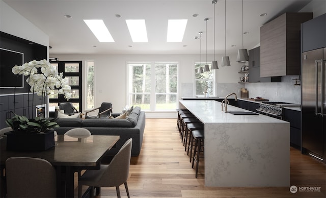 kitchen with a center island with sink, sink, a breakfast bar area, pendant lighting, and light wood-type flooring