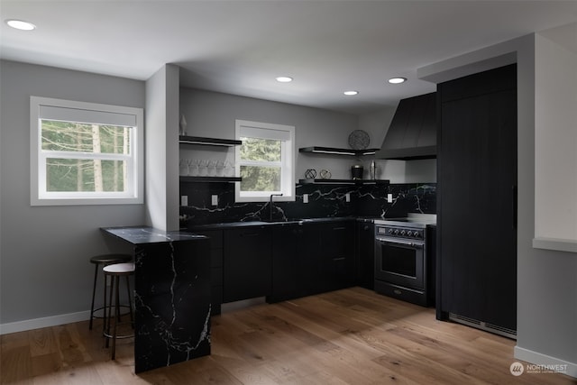 kitchen featuring light wood-type flooring, wall chimney exhaust hood, stainless steel range with electric cooktop, and backsplash