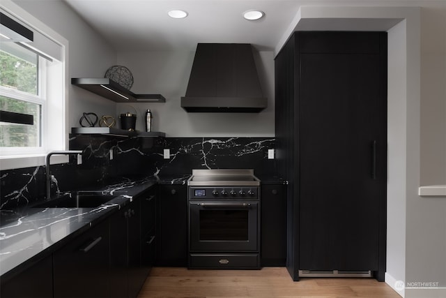 kitchen featuring stainless steel electric range, light wood-type flooring, sink, and premium range hood