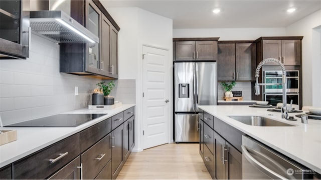 kitchen featuring tasteful backsplash, dark brown cabinets, stainless steel appliances, extractor fan, and light hardwood / wood-style flooring