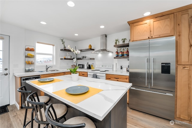 kitchen featuring a center island, stainless steel appliances, sink, wall chimney exhaust hood, and light hardwood / wood-style flooring