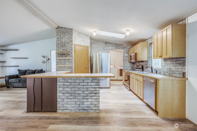 kitchen with vaulted ceiling with skylight, stainless steel appliances, light brown cabinets, and light wood-type flooring