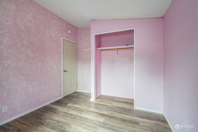 unfurnished bedroom with a closet, hardwood / wood-style floors, and vaulted ceiling