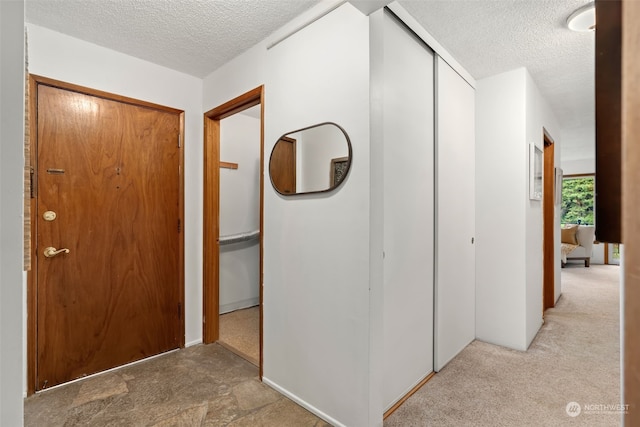 hallway with light carpet and a textured ceiling