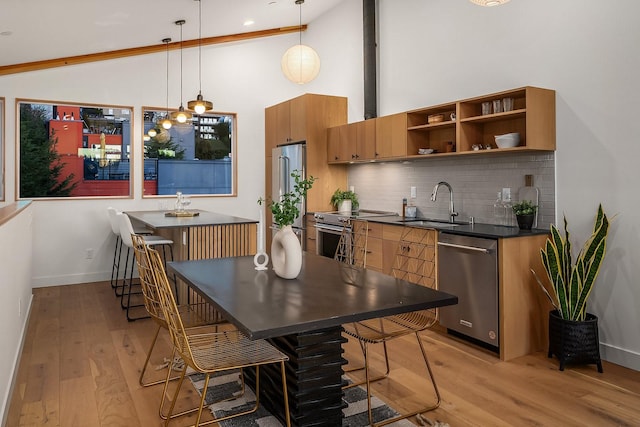 kitchen featuring sink, a kitchen breakfast bar, hanging light fixtures, stainless steel appliances, and light wood-type flooring