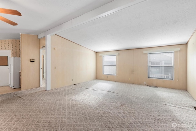 carpeted empty room with ceiling fan, wood walls, and a textured ceiling