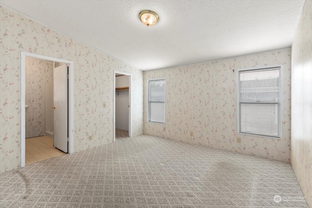 unfurnished bedroom featuring a walk in closet, ensuite bathroom, a closet, and a textured ceiling