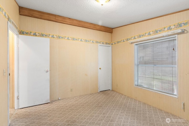 unfurnished room with light carpet, a textured ceiling, and wooden walls