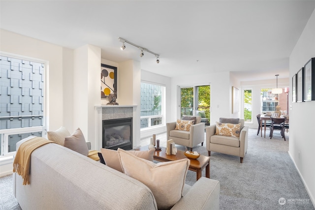 living room featuring a tiled fireplace, rail lighting, and light carpet