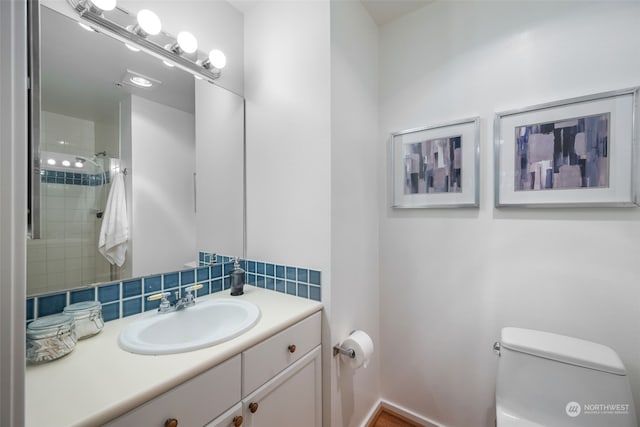 bathroom featuring vanity, toilet, backsplash, and tiled shower