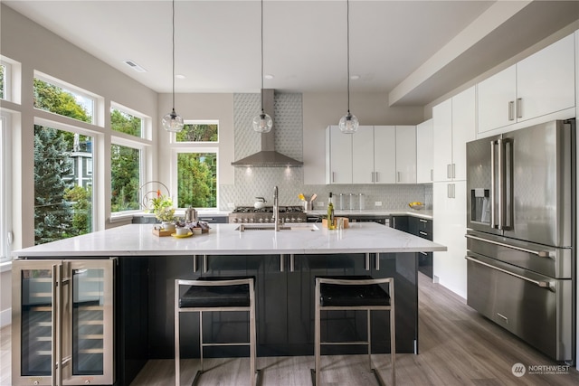 kitchen with high end refrigerator, wall chimney exhaust hood, beverage cooler, and a center island with sink