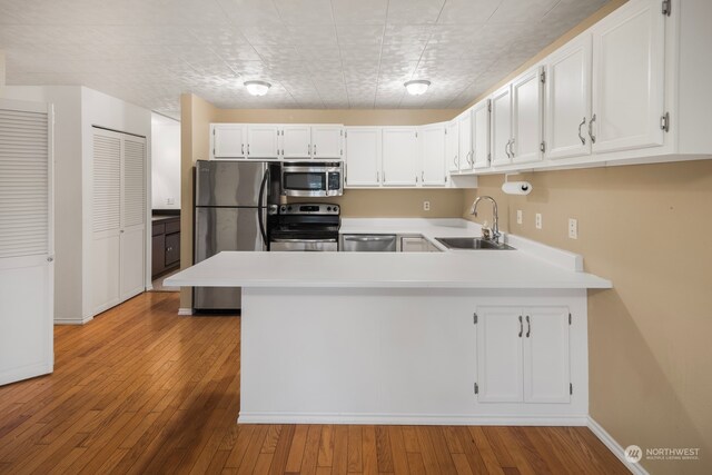 kitchen featuring white cabinetry, sink, stainless steel appliances, light hardwood / wood-style flooring, and kitchen peninsula