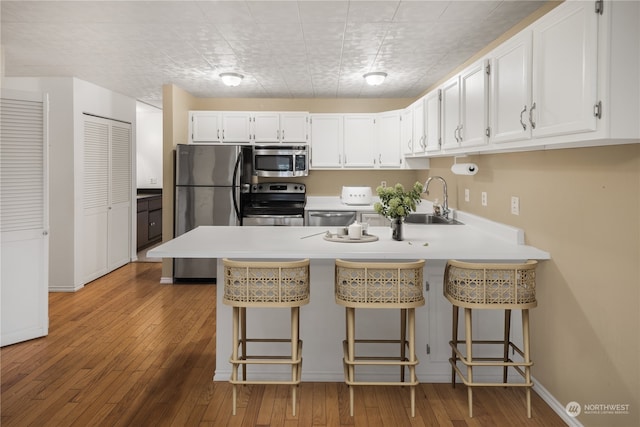 kitchen with a kitchen breakfast bar, white cabinetry, stainless steel appliances, and light hardwood / wood-style floors