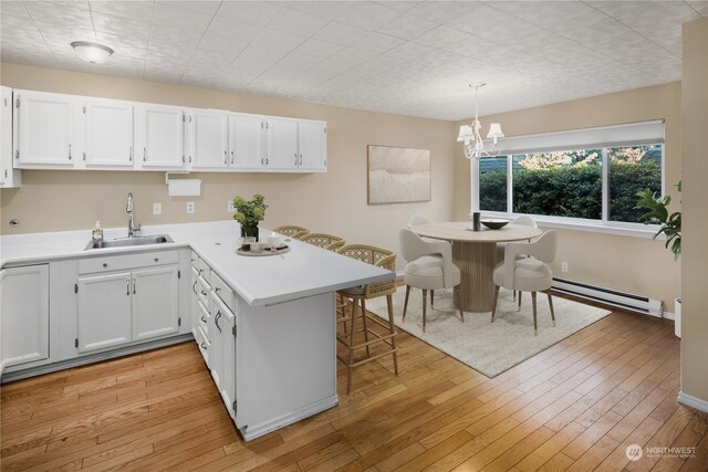 kitchen featuring baseboard heating, kitchen peninsula, white cabinets, and decorative light fixtures