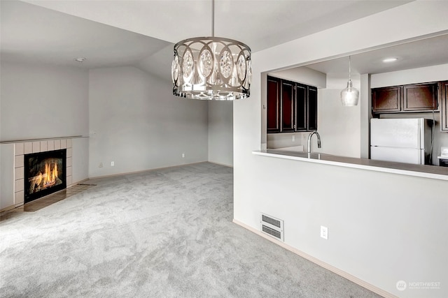 unfurnished living room with a tile fireplace, light colored carpet, lofted ceiling, and sink