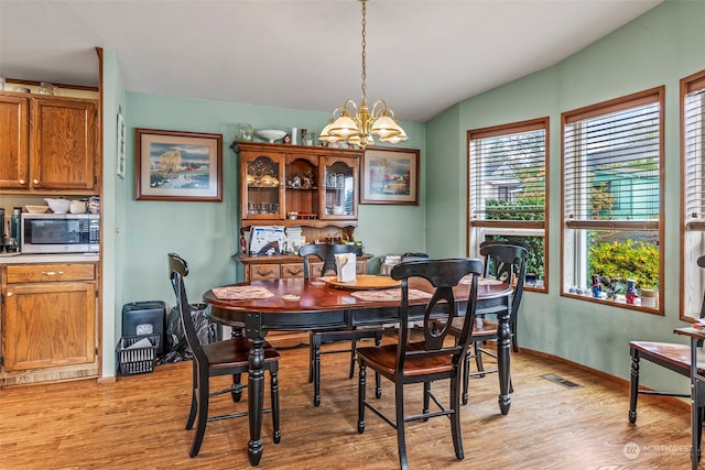 dining area featuring vaulted ceiling, an inviting chandelier, and light hardwood / wood-style flooring